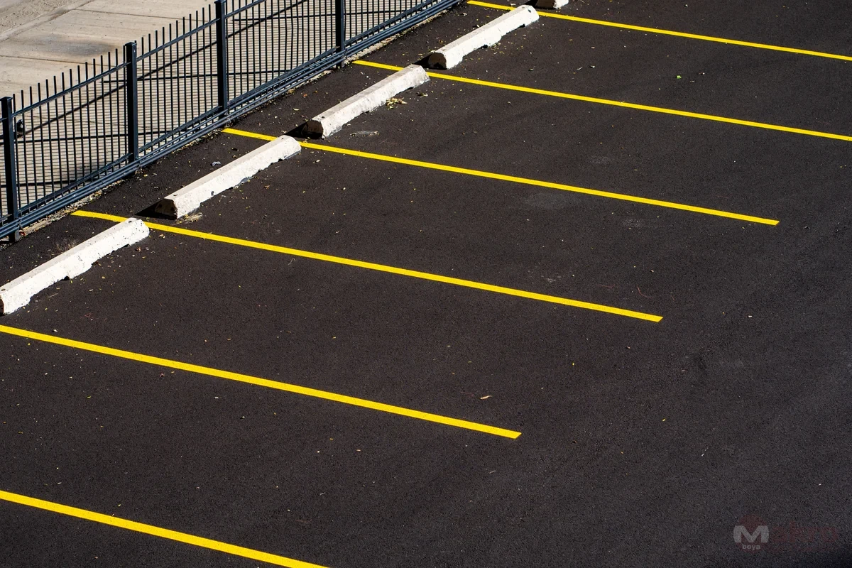 Asfalt otoparkta sarı park çizgileri, beyaz araç durdurucular ve metal çevre çiti